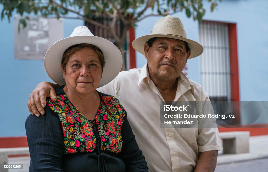 Latin couple of grandparents, sitting outdoors in colorful streets of Oaxaca, Mexico latin couple sitting and looking at camera Mexico Stock Photo