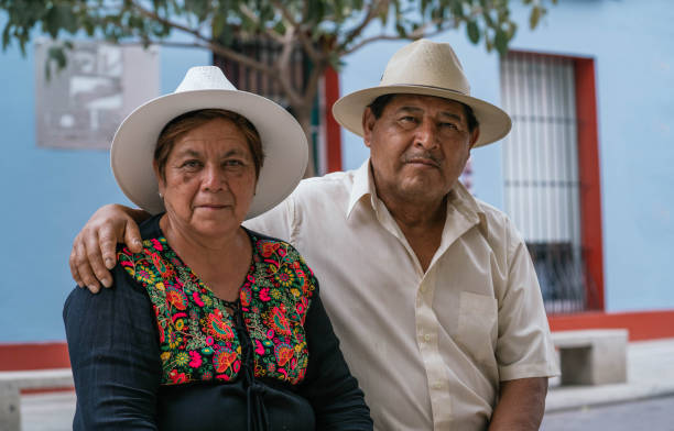 Latin couple of grandparents, sitting outdoors in colorful streets of Oaxaca, Mexico latin couple sitting and looking at camera citizenship photos stock pictures, royalty-free photos & images
