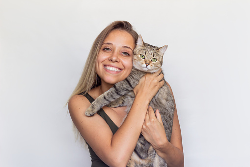 A young beautiful smiling blonde woman holds young Tabby cat in her hands isolated on a white background. Good friends. Friendship of a pet and its owner. Cuddles