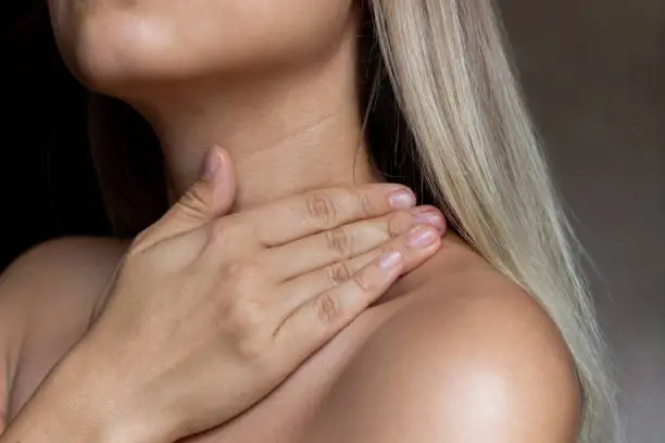 A close-up of a young blonde woman's skin. The girl uses a cream to moisturize the skin of the neck and shoulders on a dark background. Wrinkles, age-related changes, lines. Skin care