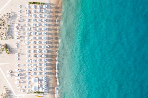 Stunning aerial view of a white sand beach bathed by a turquoise water with some relaxed people under white beach umbrellas at sunset. Cala di volpe beach, Costa Smeralda, Sardinia, Italy. Stunning aerial view of a white sand beach bathed by a turquoise water with some relaxed people under white beach umbrellas at sunset. Cala di volpe beach, Costa Smeralda, Sardinia, Italy. Cala Di Volpe stock pictures, royalty-free photos & images