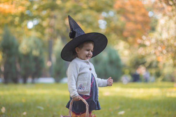 szczęśliwy haloween. portret uroczej dziewczynki w kapeluszu czarownic w jesiennym lesie. - two jack zdjęcia i obrazy z banku zdjęć