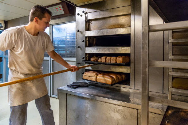 Baker taking bread out of oven stock photo