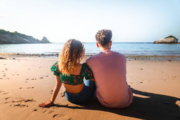encantadora pareja heterosexual en una playa rocosa abrazándose y besándose en el país vasco. - honeymoon beach couple heterosexual couple fotografías e imágenes de stock