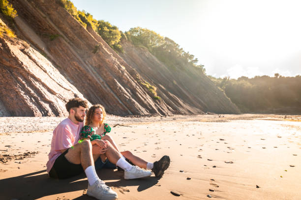 encantadora pareja heterosexual en una playa rocosa abrazándose y besándose en el país vasco. - honeymoon beach couple heterosexual couple fotografías e imágenes de stock