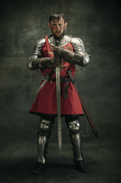 Portrait of one brutal bearded man, medeival warrior or knight with dirty wounded face holding sword Full length. Portrait of one brutal bearded man, medeival warrior or knight with dirty wounded face holding big sword isolated over dark background. body armor stock pictures, royalty-free photos & images