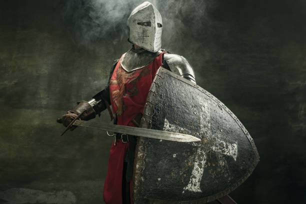 One medeival warrior or knight in armor and helmet with shield and sword Noble warrior. Portrait of one medeival warrior or knight in armor and helmet with shield and sword posing isolated over dark background. sword photos stock pictures, royalty-free photos & images