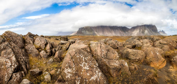 Giant panoramic view. Huge cobblestones and rock fragments in the foreground and a high Vestrahorn mountain covered with clouds on the horizon. Summer in Stokksnes, Iceland. High quality photo.
