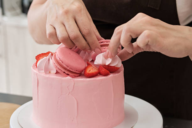 istock Woman pastry chef decorates pink cake with macaroons and berries, close-up. Cake making process, Selective focus 1333714824