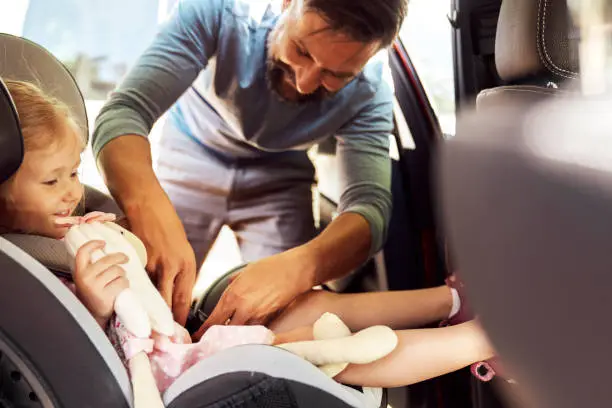 Photo of Side view of father securing child to a baby car seat