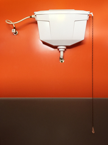 Front view old flushing toilet hanging on the orange color wall