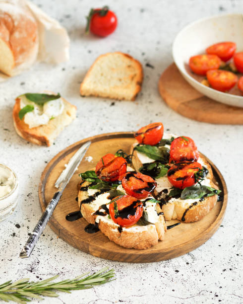 italian cuisine. bruschetta with baked tomatoes, basil and soft cheese. dressing from balsamic sauce. italian food on a white background. toasts are being prepared. baguette, rosemary, and ricotta. - vinegar balsamic vinegar modena italy imagens e fotografias de stock