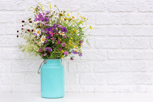 Bouquet of bright flowers in tin can vase on background white brick wall. Template for postcard. Concept Women's day, Mothers Day, Hello summer or Hello spring.