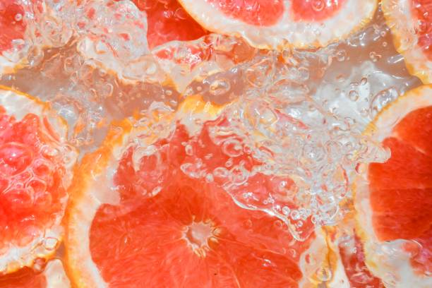 istock Slices of grapefruit in water on white background. Grapefruit close-up in liquid with bubbles. Slices of blood red ripe grapefruit in water. Macro image of fruits in water 1333726312