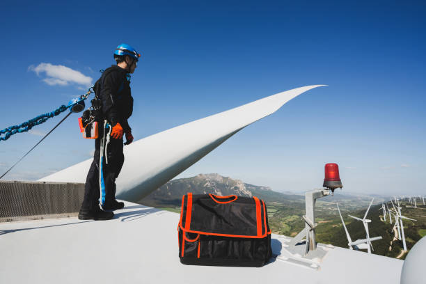 ingegnere che lavora nella parte superiore di una turbina eolica. - working windmill foto e immagini stock