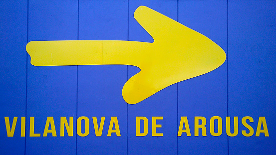 Close-up view of Vilanova de Arousa sign and pilgrims yellow arrow symbol on blue painted wooden planks in the Camino de Santiago, camino portugués.