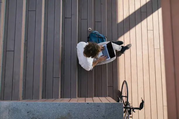 Photo of Bird's eye view of a well-dressed, young manager writing emails outdoors