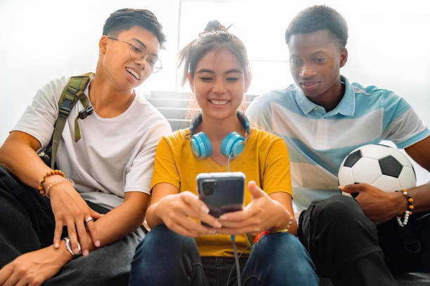 grupo multirracial de colegas adolescentes do ensino médio sentam-se nas escadas olhando para o celular de uma adolescente. - high school audio - fotografias e filmes do acervo