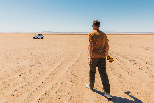 Man tourist going to the car with roof top tent at the warm sand during sunny day at Namib-Naukluft national park, Southern Africa