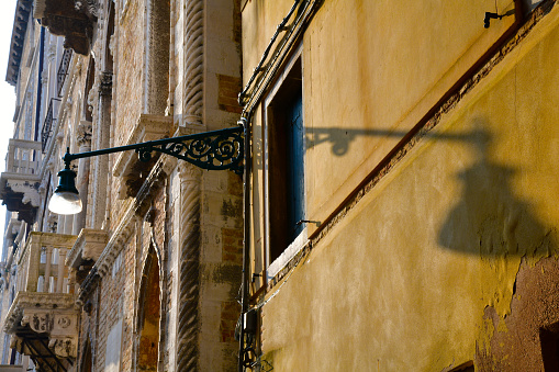 Low angle view of a retro streetlight in Venice, Italy fixed on old building throwing a shadow on yellow wall of adjacent house