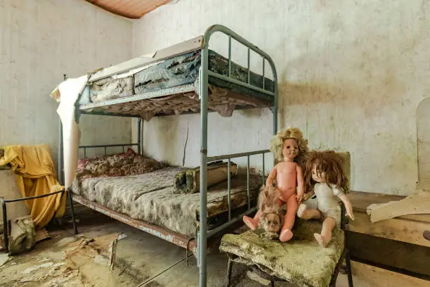 Decayed bedroom in pastel shades with 3 dolls, haunting scene