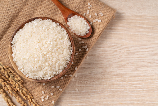 White raw rice in a bowl with the ear on the wooden table background.