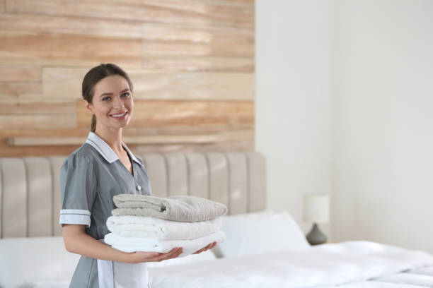 istock Young chambermaid holding stack of fresh towels in bedroom. Space for text 1333741284