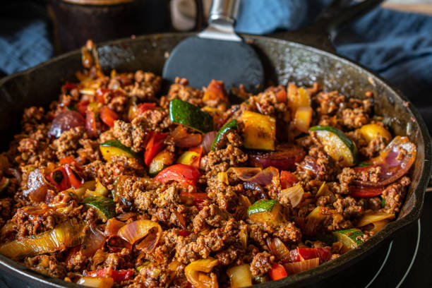 Pan fried ground beef with vegetables Delicious spicy and low carb pan dish with low fat ground beef and mediterranean vegetables served hot in a rustic cast iron pan on table background. Closeup view skillet stock pictures, royalty-free photos & images