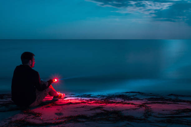 istock Young man sitting on moonlit beach with flashlight, long exposure 1333747394