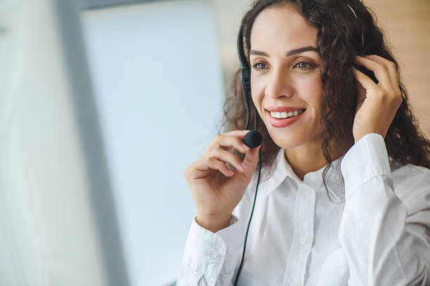 Young friendly operator woman agent with headsets. Beautiful business woman wearing microphone headset working in the office as a telemarketing customer service agent, call center job concept. stock photo