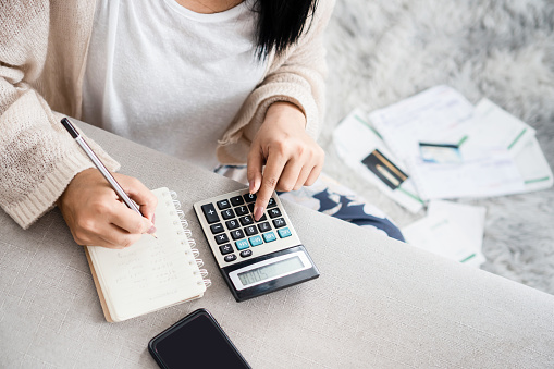 mujer escribiendo una lista de deudas en el cuaderno calculando sus gastos con la calculadora photo