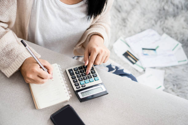 wanita menulis daftar utang pada notebook menghitung pengeluarannya dengan kalkulator - anggaran belanja potret stok, foto, & gambar bebas royalti