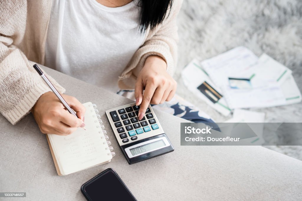 woman writing a list of debt on notebook calculating her expenses with calculator woman writing a list of debt on notebook calculating her expenses with calculator with many invoices , female hand doing accounting Calculator Stock Photo