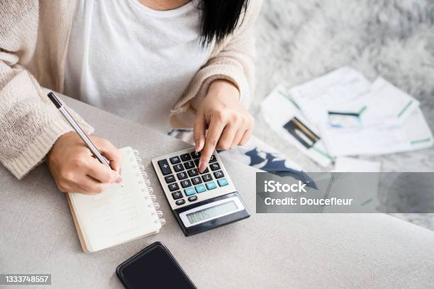 Woman Writing A List Of Debt On Notebook Calculating Her Expenses With Calculator Stock Photo - Download Image Now