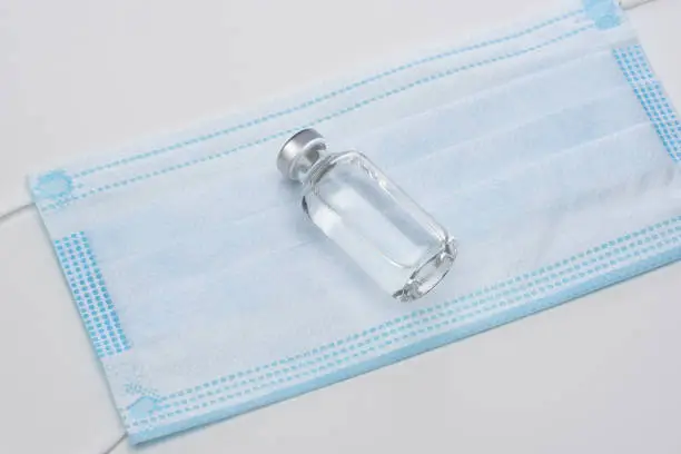Covid-19 Concept. A vial of injectable medicine or vaccine on a surgical mask. The bottle has no label.