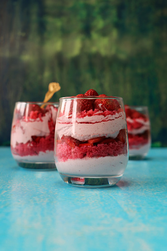 Stock photo showing a close-up studio shot of a glasses containing layered, strawberry mousse desserts topped with whole strawberries.