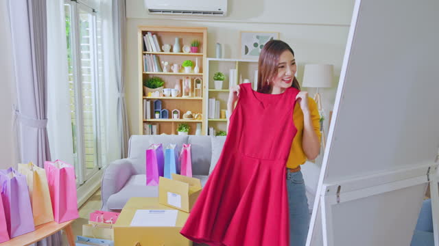 happy asian woman trying on new dress from opened delivery box by mirror at home in slow motion