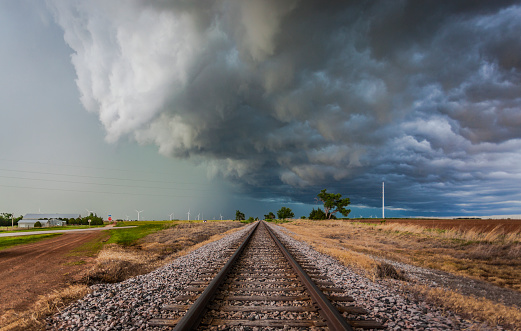 Severe storm with torrential rain shaft and lowering over railroad tracks and farmland with wind turbines in distance: Image taken from the safety of a public railway/road crossing