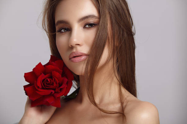 istock Pretty woman holds red rose flower by chin looking at camera 1333762000