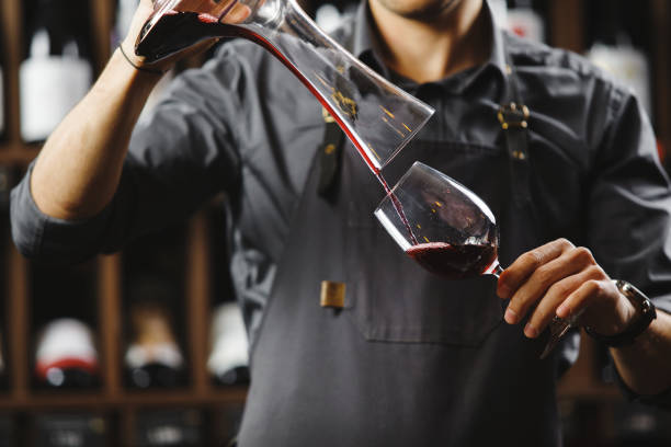 istock Bartender pours red wine in glass from big transparent vessel 1333765653