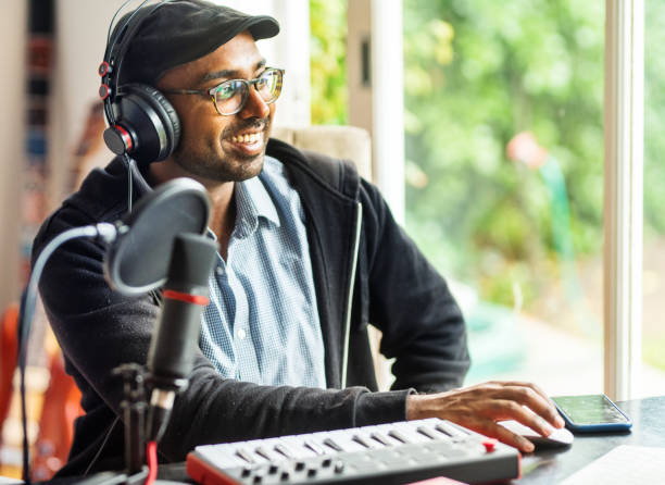 young man laughing while doing a podcast in his home studio - indian ethnicity audio imagens e fotografias de stock