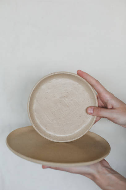 istock Hands holding ceramic plates isolated on white background. Minimalist set of handmade ceramic tableware and pottery 1333772518