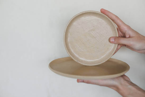 istock Hands holding ceramic plates isolated on white background. Minimalist set of handmade ceramic tableware and pottery 1333772610