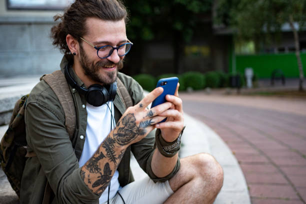 jovem moderno na rua da cidade usando telefone inteligente - mid adult men smart casual white happiness - fotografias e filmes do acervo