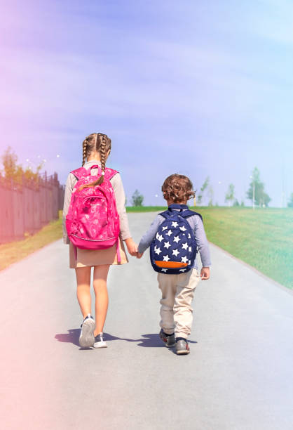istock Two schoolchildren with backpacks are walking along the road 1333776326
