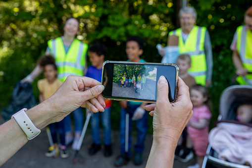 Group of adults and children posing for a group photo together that a woman is taking on her mobile phone while out litter picking in their community in the North East of England. The adults are wearing a high vis jackets and they are all of different ages.