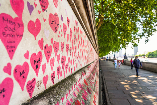 London, UK - A close-up showing dedications written on the hundreds of thousands of red hearts painted on the wall along the South Bank of the Thames in central London, with each heart representing a victim of the Covid-19 pandemic in the UK.