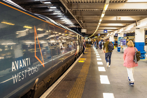 London, UK - Passengers walking on a platform at Euston Station, alongside an Avanti West Coast train.