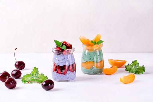 Chia pudding with spirulina and matcha tea powders topped with cherry and apricot and served in glass jars. Healthy dessert