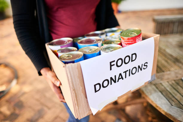 Close-up of a young woman carrying a box of food donations Close-up of a young woman standing outside with a box of food donations for a charitable cause canned food stock pictures, royalty-free photos & images